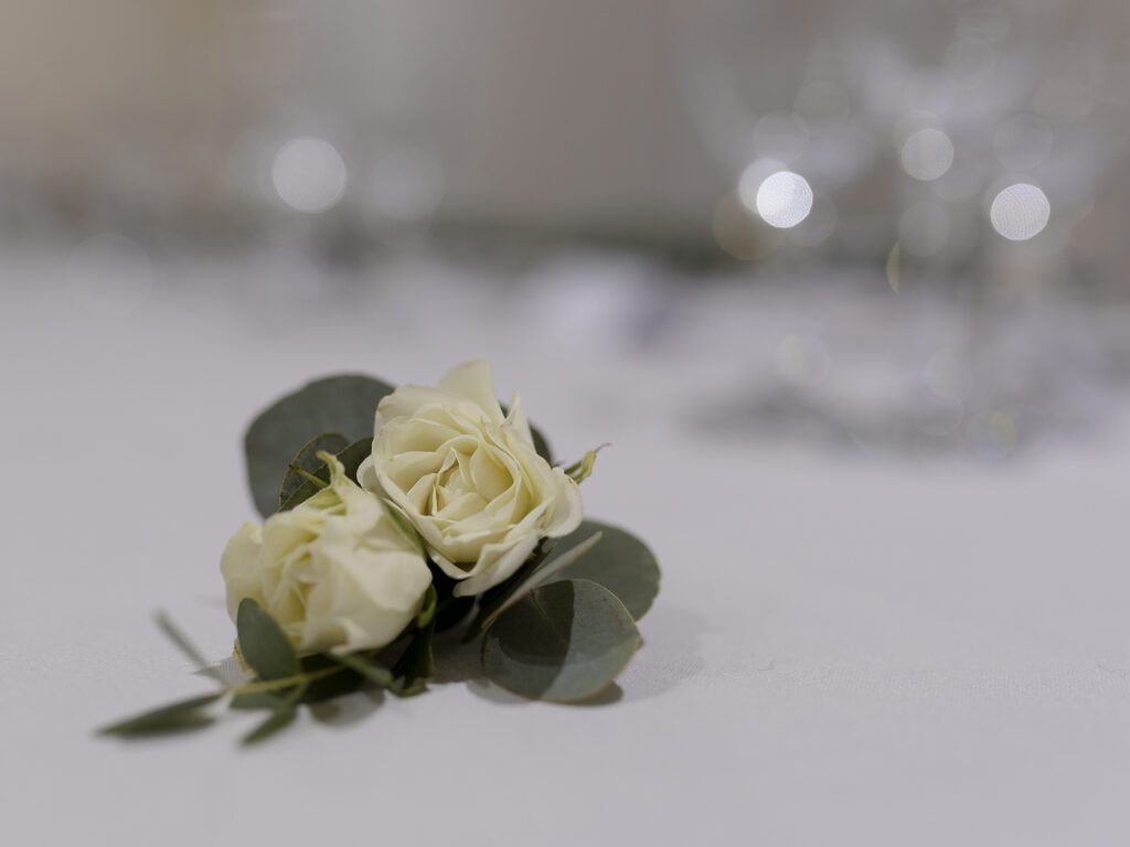 Grooms white/ivory rose button hole is laid on a table.