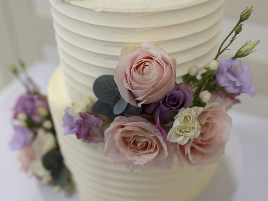 Wedding cake showing real flower decorations. The flowers match the bridal bouquet of pale pink, purple and ivory roses.