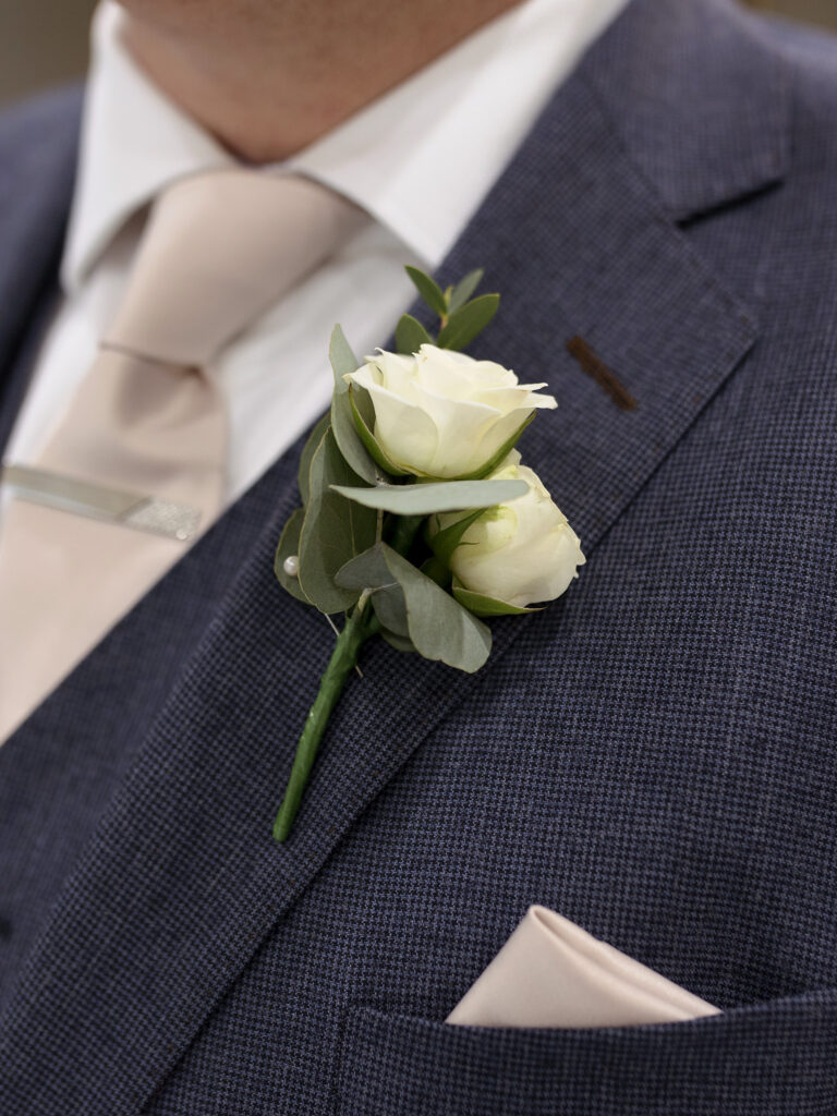 A close up of a grooms ivory rose button hole. 