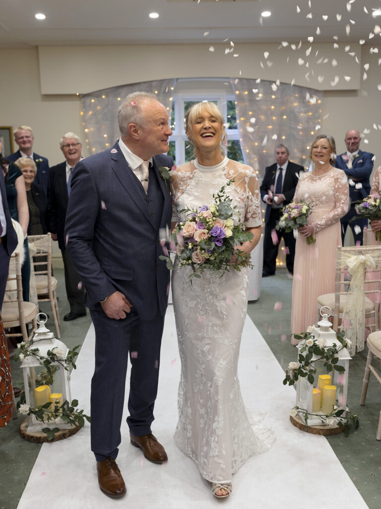 A bride and groom at The Petwood Hotel are walking back down the aisle and are being showered with confetti