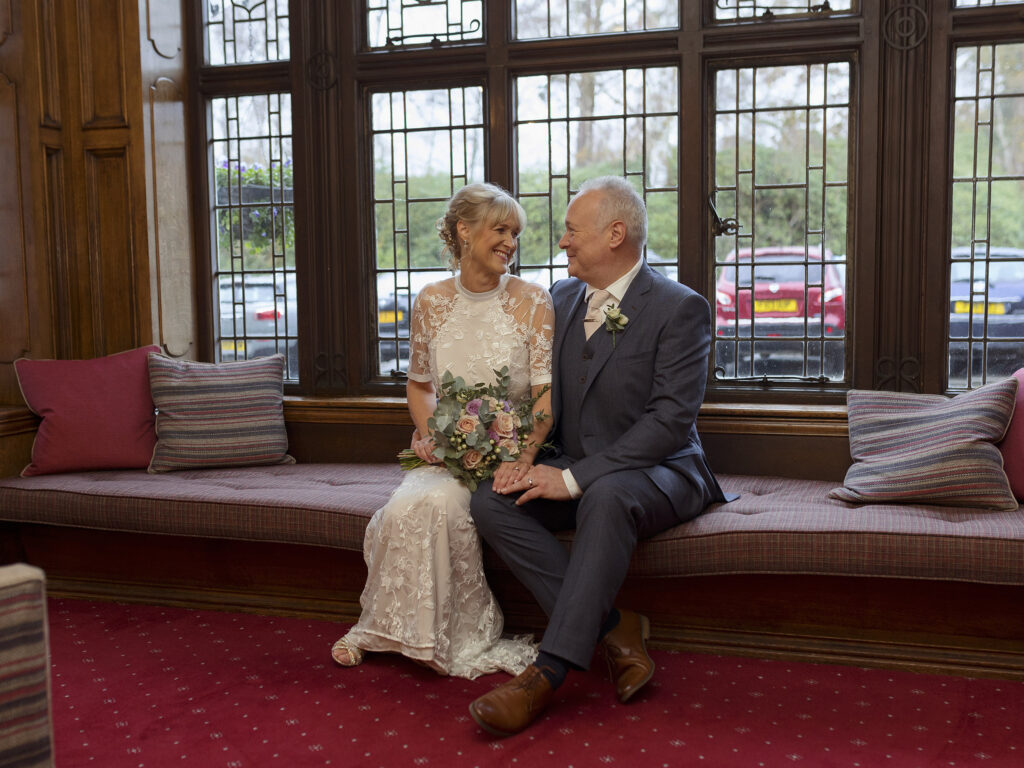 Bride and Groom are sat in front of a large window of The Petwood Hotel