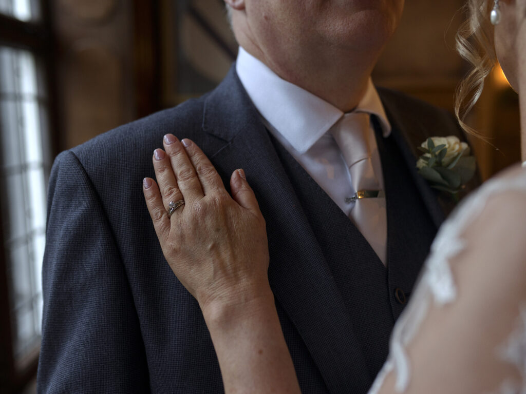 Close up of a brides wedding ring as she lays her hand on her husbands suited chest