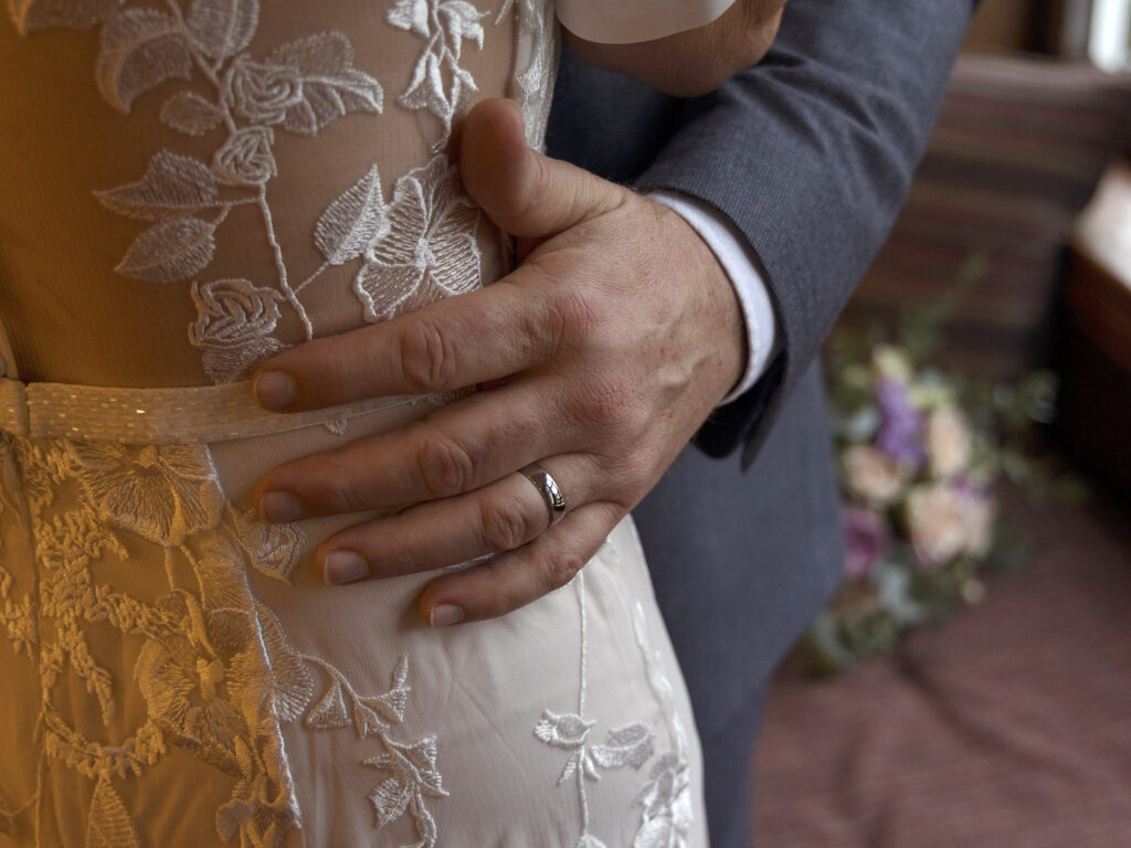 Close up of a grooms wedding ring as he holds his wife around her waist