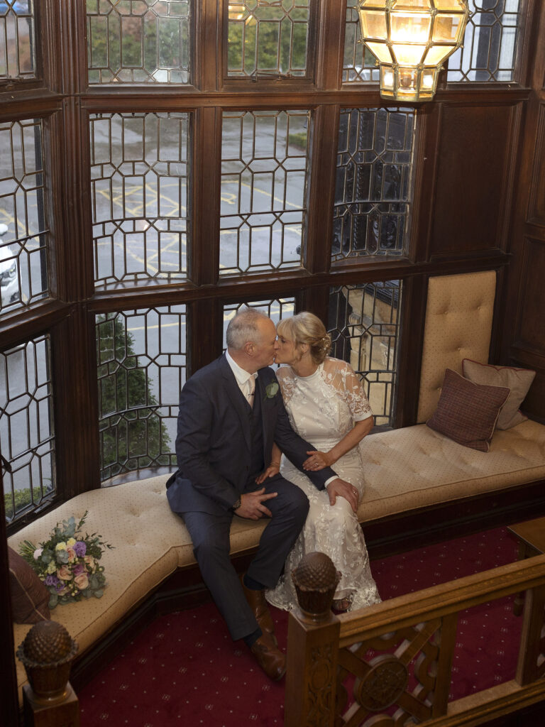 Bride and Groom are sat kissing in front of a large window of The Petwood Hotel
