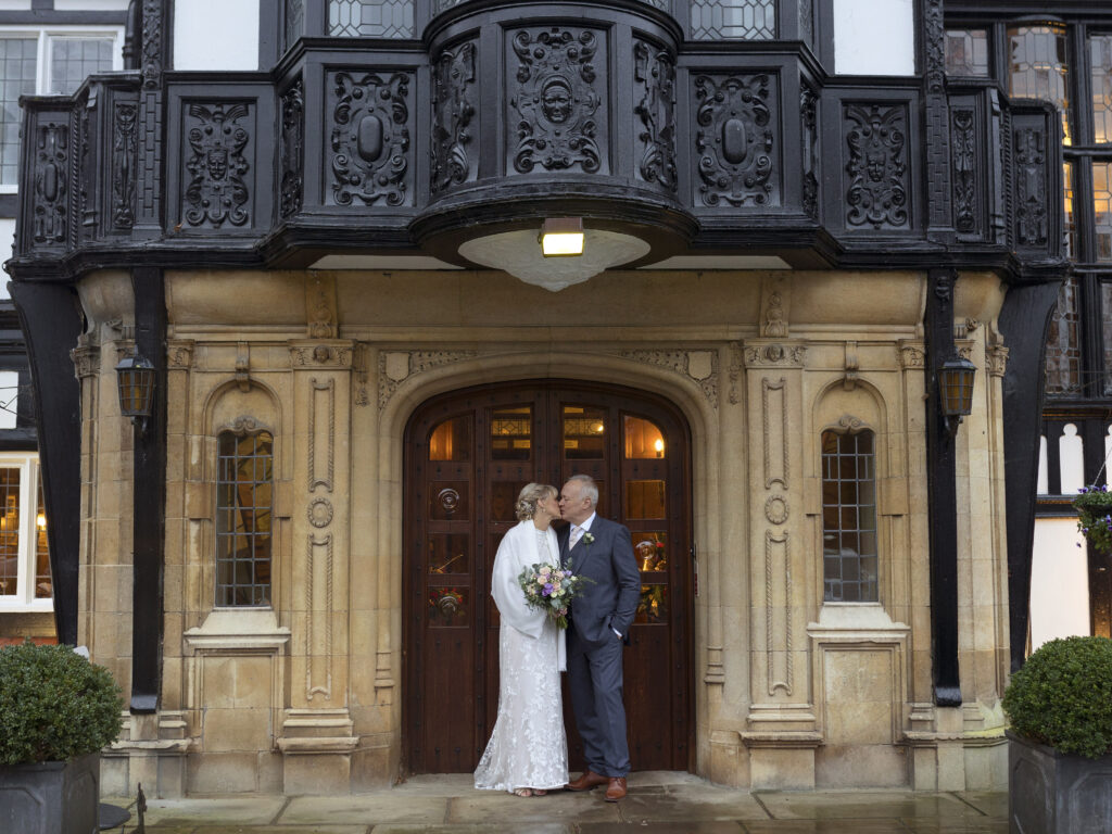 Bride and Groom stood in the doorway of The Petwood Hotel kissing. The building is a Tudor stye