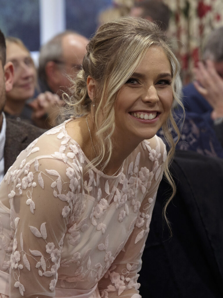 A bridesmaid is leaning forwards laughing and smiling at the camera