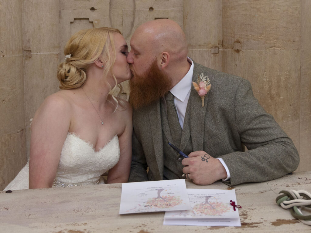 Bride and groom are sat down kissing after signing a marriage certificate at wollaton hall