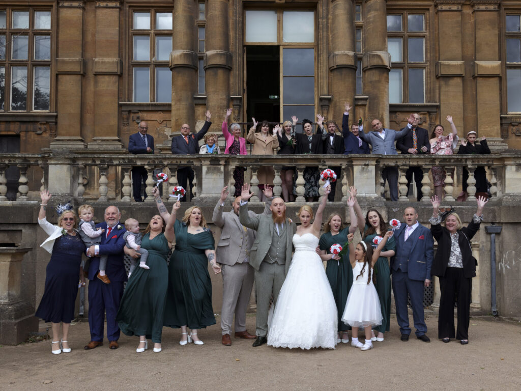 Wedding guests are stood on the balcony of Wollaton hall cheering