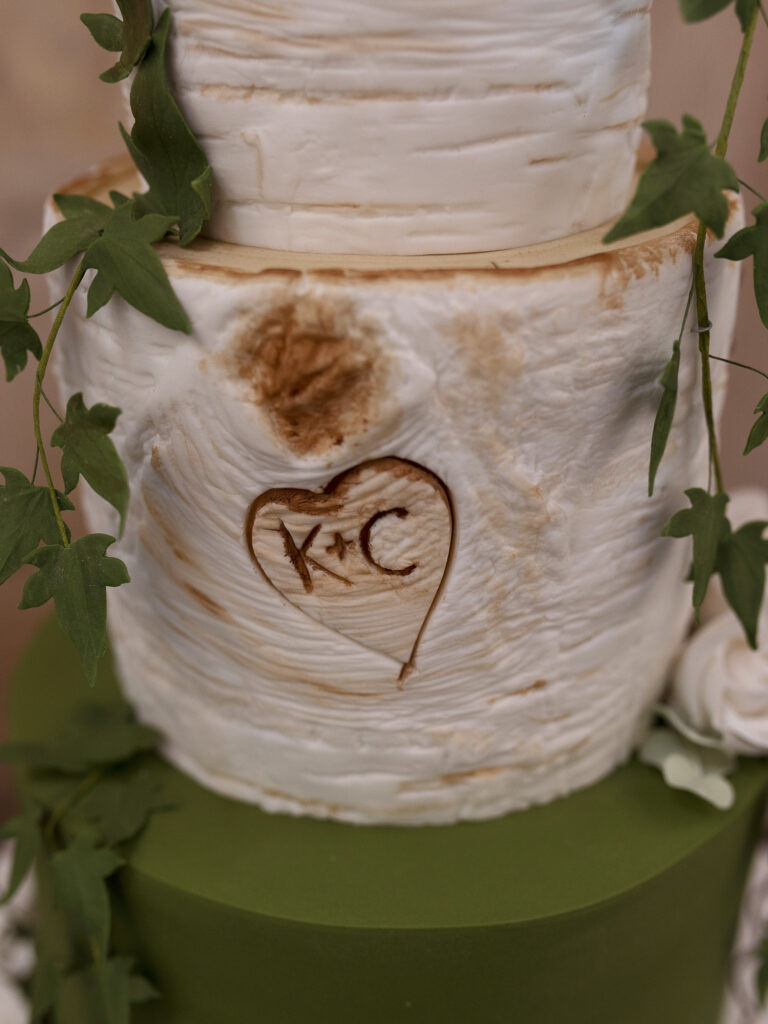 Close up of a wedding cake. It is a rustic wooden log design with K+C initials carved inside a heart