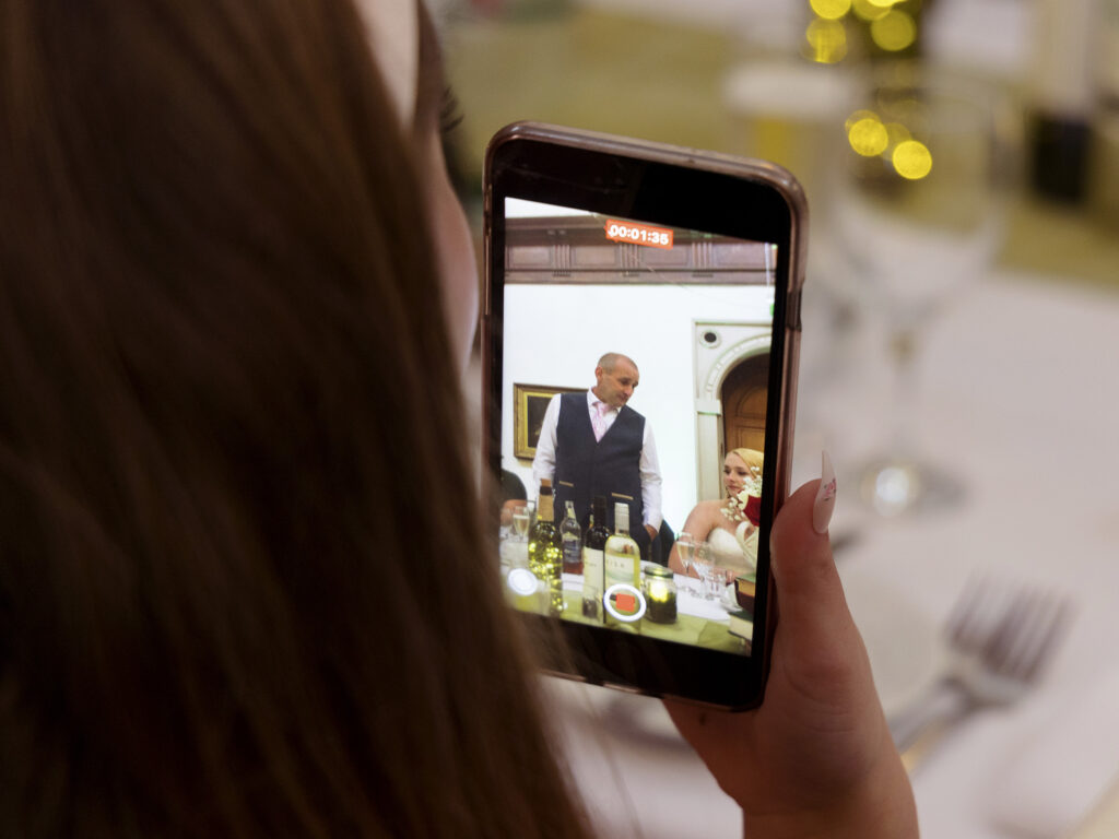 A guest is holding her mobile phone and filming the speeches. Close up of her hand and phone