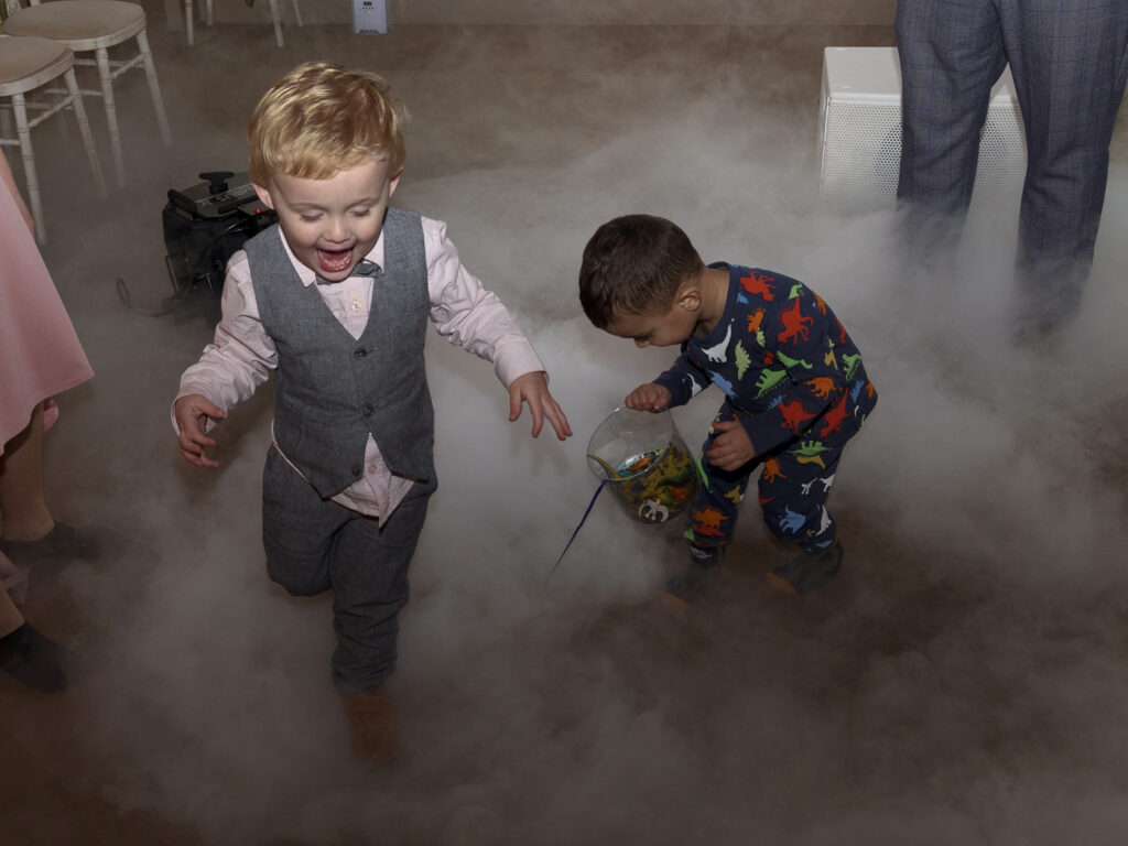 Dancefloor at a wedding at Wollaton Hall.  A little boy is running around laughing and another is collecting dinosaur toys off the dancefloor while wearing dinosaur pyjamas