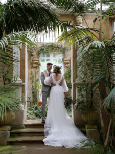 Bride and groom stood facing each other in the conservatory in Harlaxton Manor as part of the Modern Greenery Wedding At Harlaxton Manor