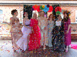 Beauty in Diversity shoot. A group of diverse women with various hidden diabilities stand together cheering, smiling and shrowing confetti