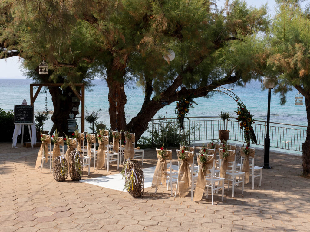 view of the outdoor destination wedding ceremony area. Rows of chairs with hessian sashes face towards the sea