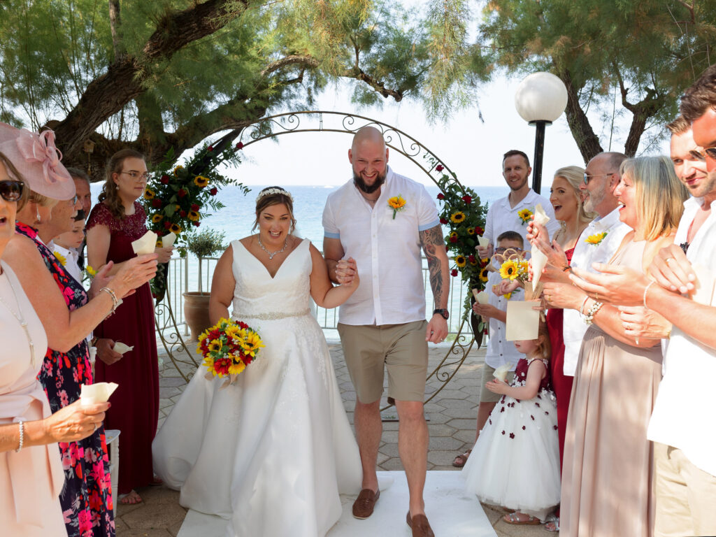Bride and groom walk back down the aisle in Zante. friends and family are stood down either side cheering