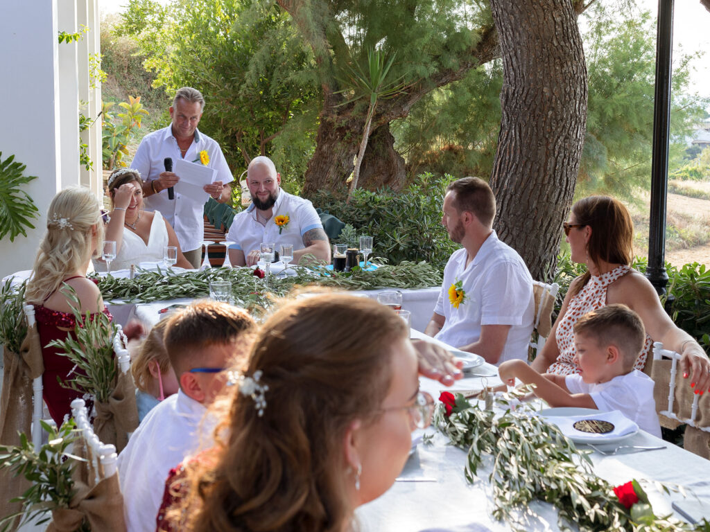 Zante destination wedding. The guests are sat at the tables, a speech is being read and the couple are reacting to what's being said