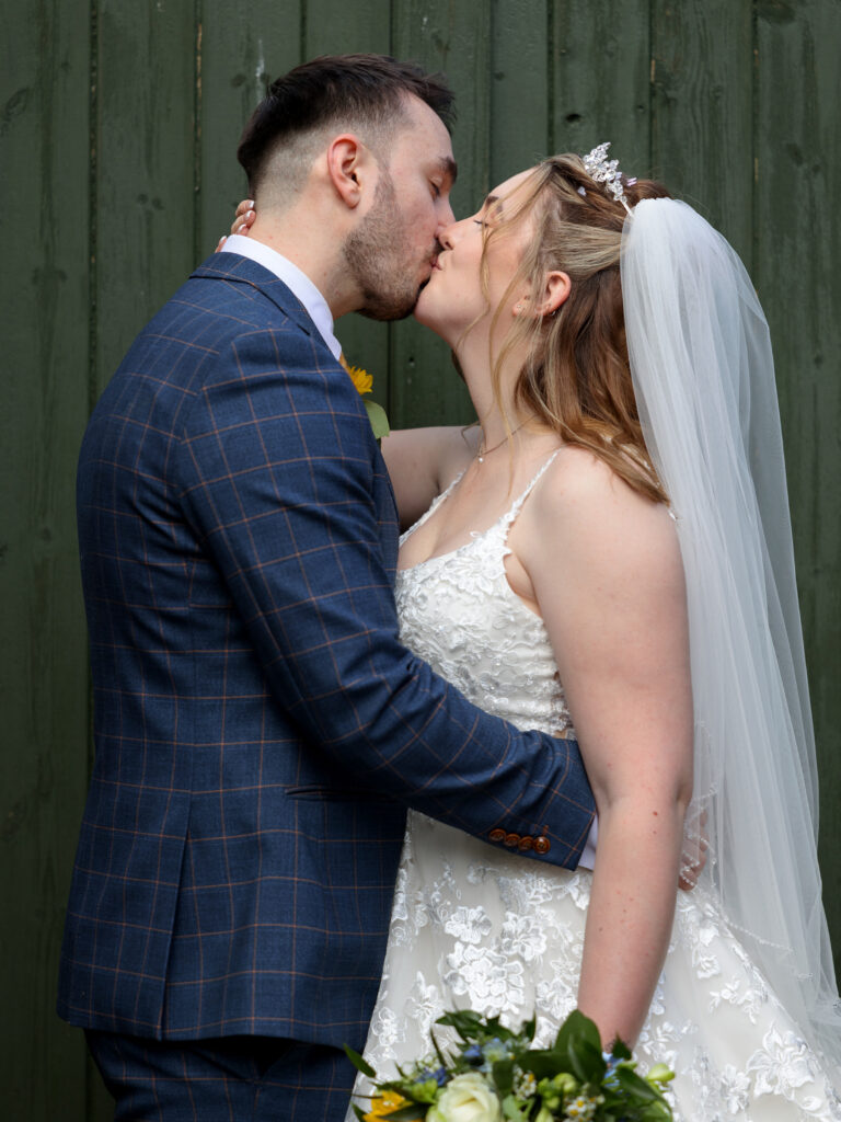 Bride and Groom kissing in front of a green wooden gate