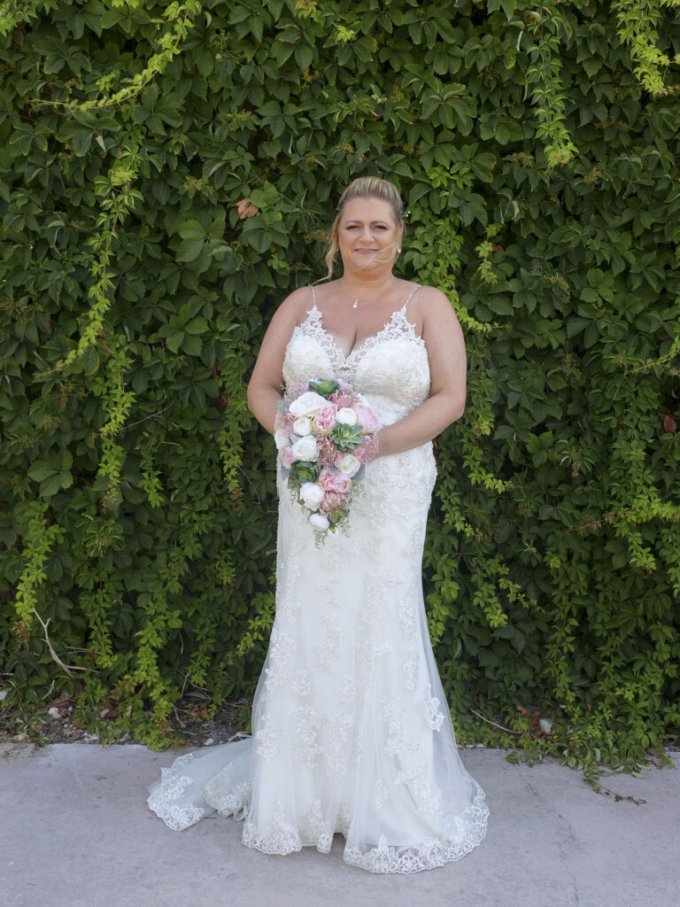 Bride stood in front of a wall of green foliage waiting to walk down to the beach for her destination wedding