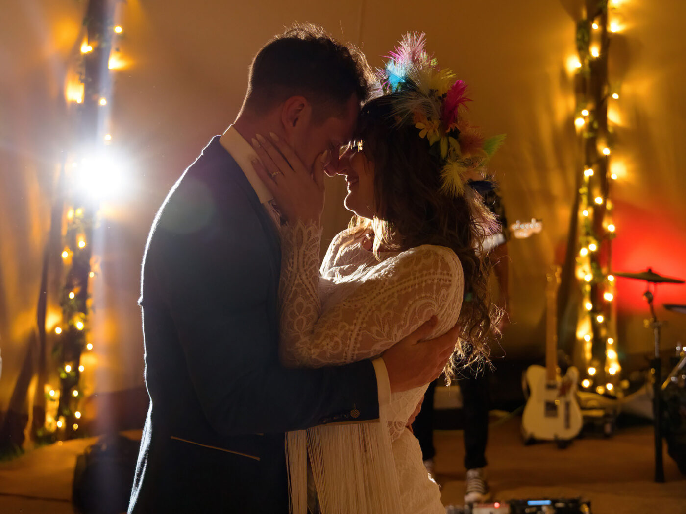 Bride and groom share an intimate first dance under warm fairy lights, foreheads touching.