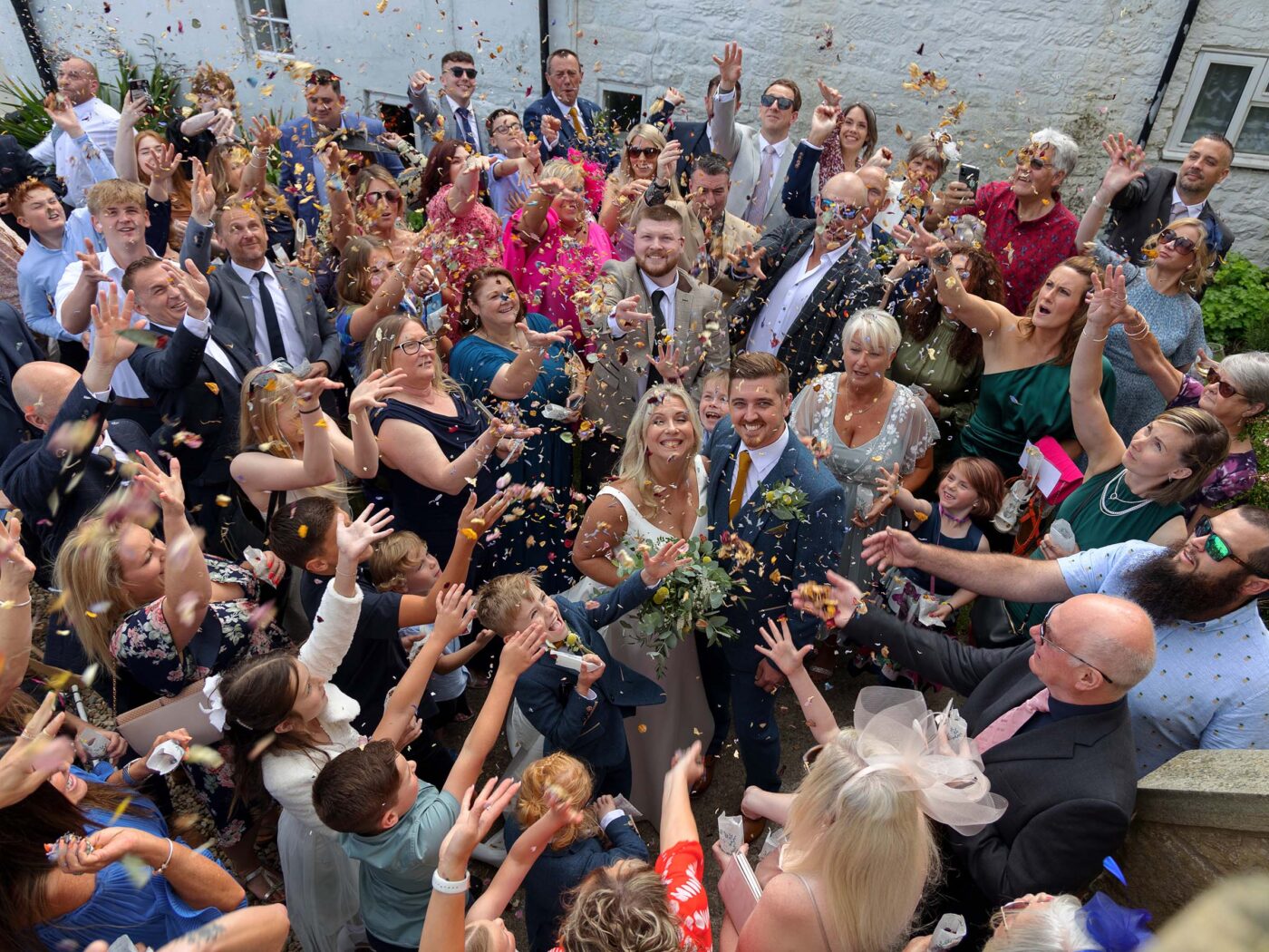 COverhead view of a bride and groom surrounded by cheering guests throwing colourful confetti into the air.