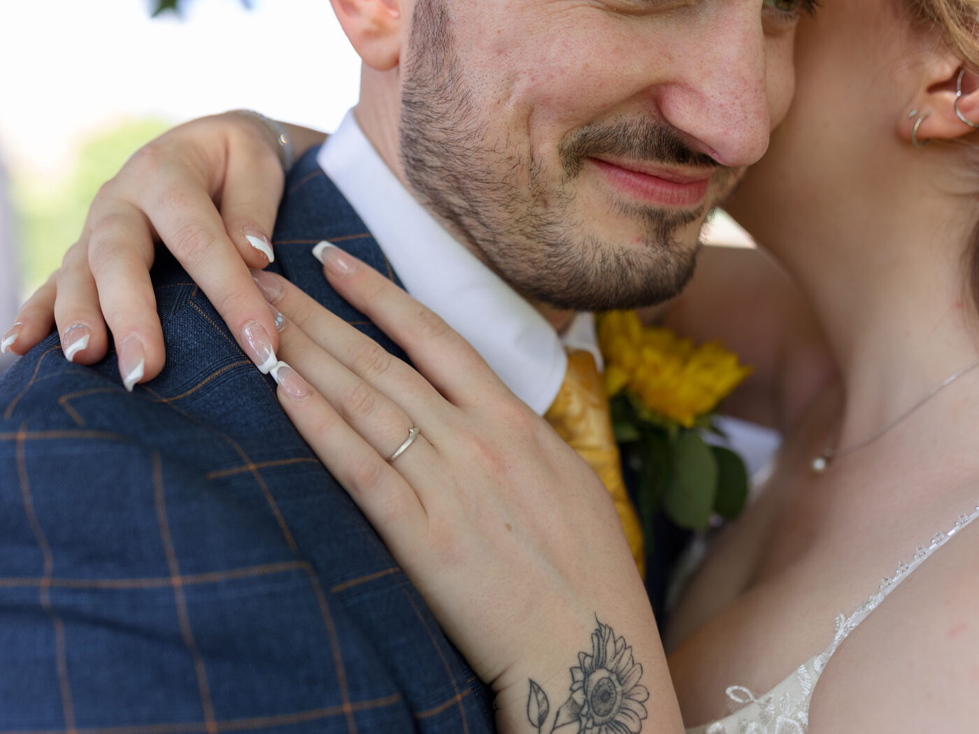 Close-up of a bride resting her hand with a wedding ring on the groom’s shoulder as they embrace.